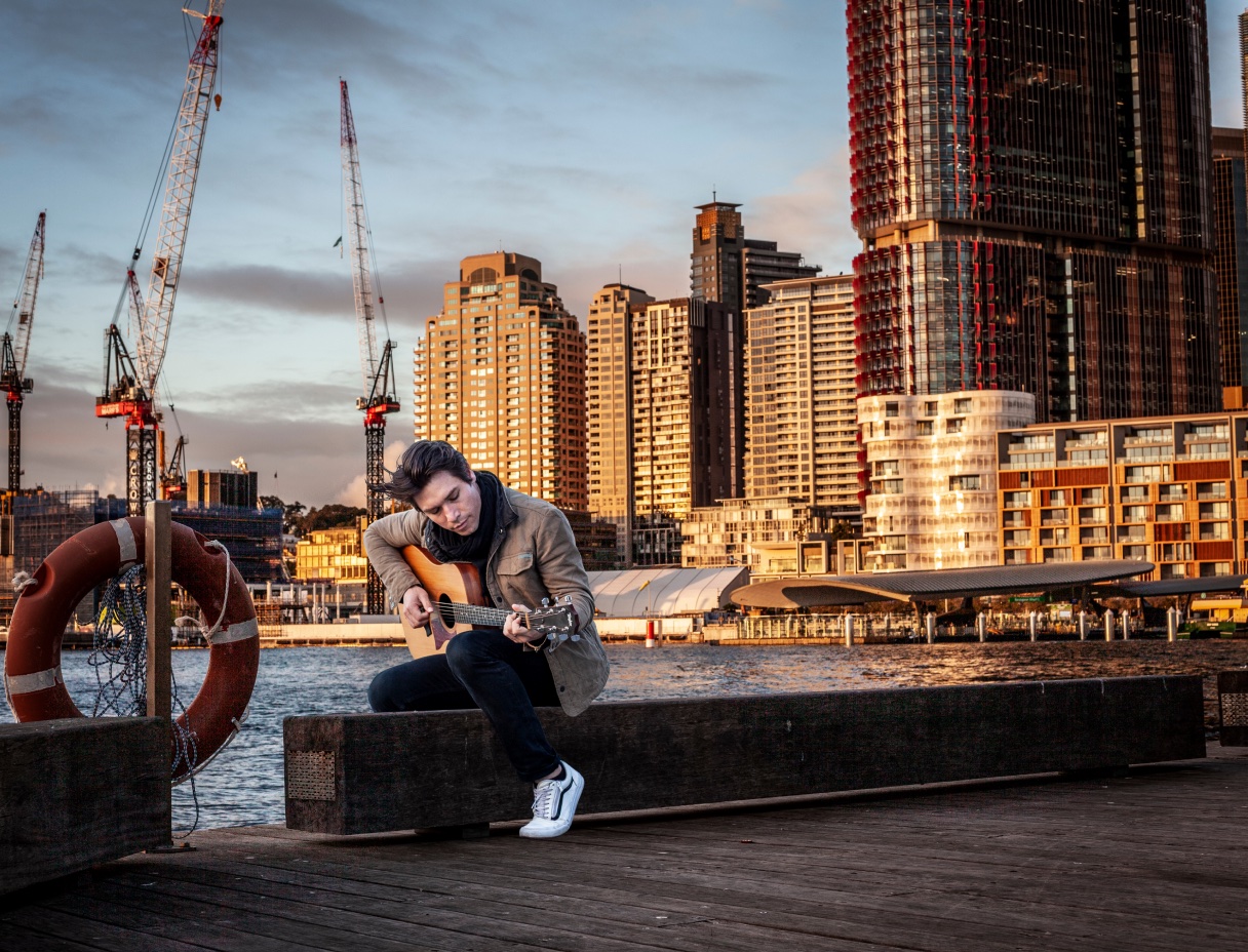 Student playing guitar on a pier in an urban center.