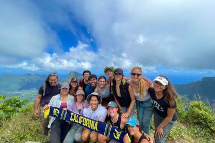 Group of students smiling at camera on top of green covered mountain