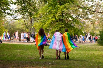 3 students with various prode flags on their back walking towards a group of people