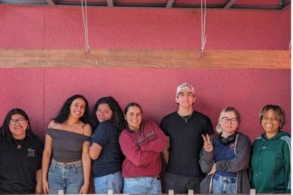 Students posing smiling in front of red cement wall