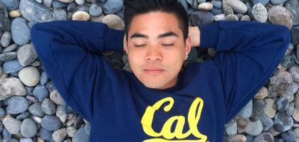 Ramil laying on back with eyes closed, wearing Cal shirt